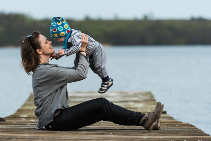 mother holding infant while on a dock by the lake